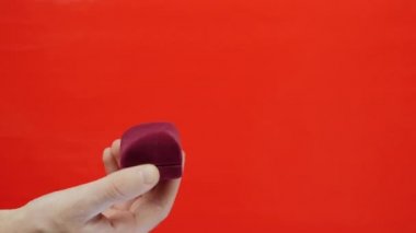 Kırmızı arka planda alyansı olan el ele tutuşma kutusu. Adam evlenme teklifi için kırmızı kutuyu tutuyor. Sevgililer Günü için hediye. Erkek küçük kırmızı kutuyu tutuyor.