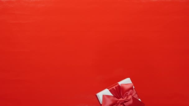 女性の手は赤い背景に赤い弓でギフトの休日の箱を与えている。女性の手は男性の手に赤いサテンの弓とお祝いの箱で贈り物を与えます。バレンタインデー誕生日の休日 — ストック動画