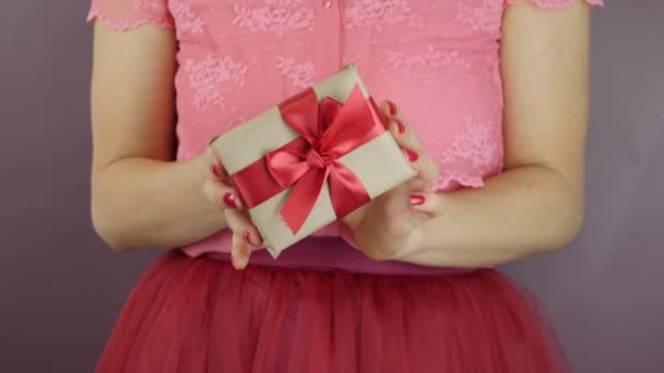 Kobiece dłonie pokazują prezent pudełko z czerwoną wstążką łuk, zbliżenie. Zapakowane w papierowy prezent rzemieślniczy z wiązaną kokardą na Walentynki, Urodziny lub Międzynarodowe Dni Kobiet. Obecny urlop — Wideo stockowe