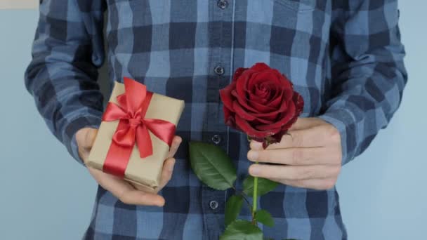Чоловік тримає подарунок і червону троянду в руках на День святого Валентина, День народження або Міжнародний жіночий день. Помазаний у папір для ремесел і краватку лук подарунковий ящик у руках чоловіків. Відпустка — стокове відео