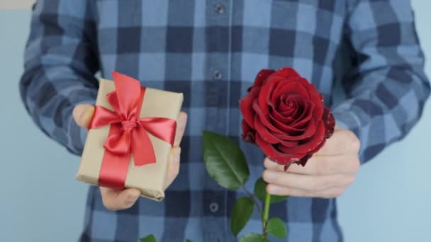 Las manos están dando regalo envuelto presente con lazo rojo atado, se mueve hacia la cámara, de cerca. El hombre sostiene una pequeña caja de regalo y se levantó en las manos para el Día de San Valentín o el Cumpleaños — Vídeos de Stock