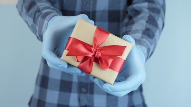 青い保護医療用手袋の手はギフトボックスを包まれて保持します。流行の冬の休日のお祝い。聖バレンタインの日のプレゼント。検疫衛生 — ストック動画
