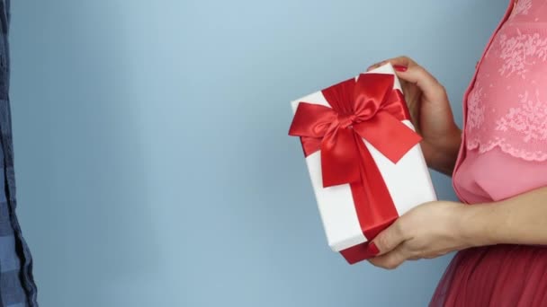 Man is receiving present gift with red ribbon bow for Birthday or Valentine's Day. Female hands are giving gift box with tied bow to male, close up. Holiday presents — Wideo stockowe