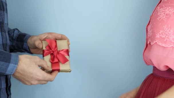 男性はバレンタインデーに女性に贈り物をしています。男性の手が保持され、女性に赤いリボン弓で包まれたギフトボックスを与えます。誕生日や国際女性デーにプレゼント。休日のコンセプト — ストック動画