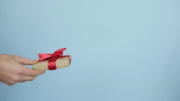 Mužská ruka drží a ukazuje dárkovou krabici s červenou stuhou na den svatého Valentýna nebo narozeniny. Muž dává zabalený dárek na modrém pozadí. Dárek k dovolené — Stock video