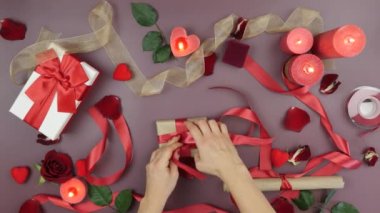 Eller, Sevgililer Günü için el işi kağıt ve kırmızı kurdeleyle hediye paketi hazırlıyor. Kadın, Sevgililer Günü için hediye kutusunu güller, mumlar ve şöminelerle süslüyor.