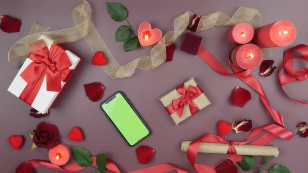 Digitales Smartphone mit grünem Chromaschlüssel auf festlichem Hintergrund mit Rosenblättern, brennenden Kerzen und Geschenken zum Valentinstag. Konzept des Online-Shoppings zum Valentinstag — Stockvideo