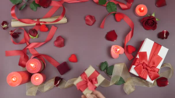 A mão masculina está dando caixa de presente embrulhada com laço vermelho amarrado à mão feminina para o Dia de São Valentim contra fundo festivo com rosas e velas. Mulher está recebendo presente presente do homem — Vídeo de Stock