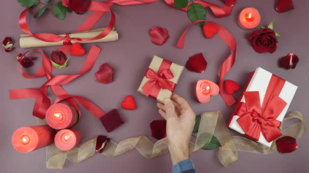 Man gives present to woman. Present gift box wrapped with red ribbon and craft paper. Valentine's Day gifts on festive table background with candles, roses and hearts — Wideo stockowe