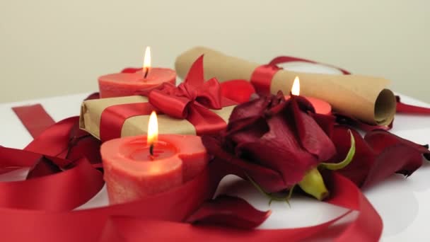 St. Valentine's Day decorations. Celebration of 14th of February. Holiday surprise. Romantic greeting. Burning candles, roses petals and gift presents are rotating on white background. — Wideo stockowe