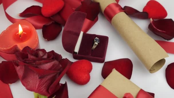 Engagement ring in opened red box on white background with romantic decoration. Roses petals, burning candles and romantic gift are rotating on white background. St. Valentine's Day surprise — Stok video