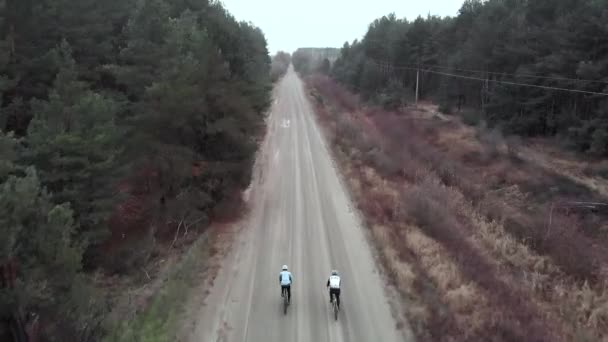 Два велосипедиста едут на гравийных велосипедах по пустой лесной дороге. Активные туристы изучают новые районы на велосипедных дорогах — стоковое видео