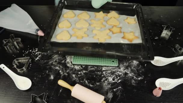 Les mains féminines mettent un plateau de four avec des biscuits au pain d'épice cuits au four sur une table en bois noir. Femme enlève les biscuits cuits sur la plaque de cuisson du four. Boulangerie festive pour la Saint-Valentin ou Noël. — Video