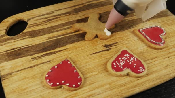 Femme essaie de glaçure pain d'épice homme, fermer. Les mains décorent des biscuits sucrés pour la Saint-Valentin ou Noël. Vitrage de biscuits faits à la main à la maison cuisine — Video