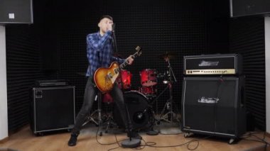 Gitarist elektro gitarda solo gitar çalıyor ve şarkılar söylüyor.