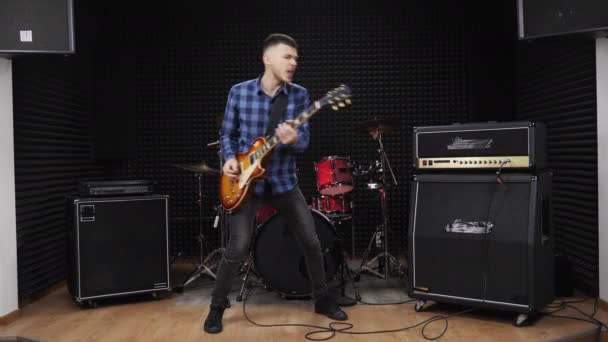 Радісний рок-гітарист виконує емоційне соло на електрогітарі у студії. — стокове відео