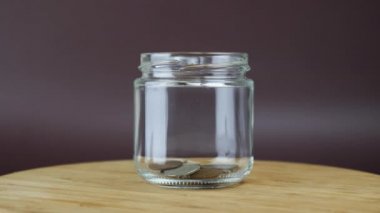 Bir yığın bozuk para cam para kutusuna düşüyor. Kişi cam kavanoza bozuk para koyar.