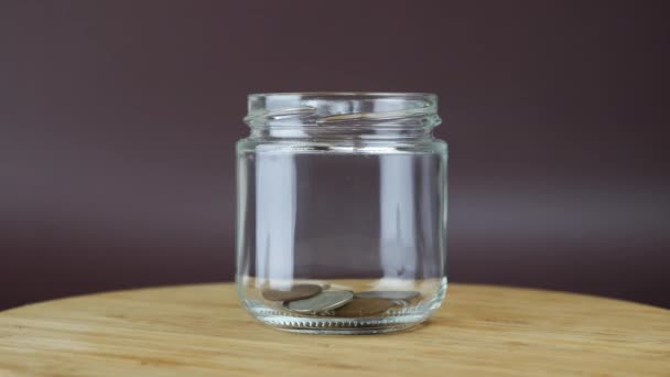 Stack of coins are falling in glass moneybox. Person puts coins into glass jar — Stock Video
