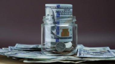 El, 100 dolarlık banknotu cam kavanoz para kutusuna koyuyor.
