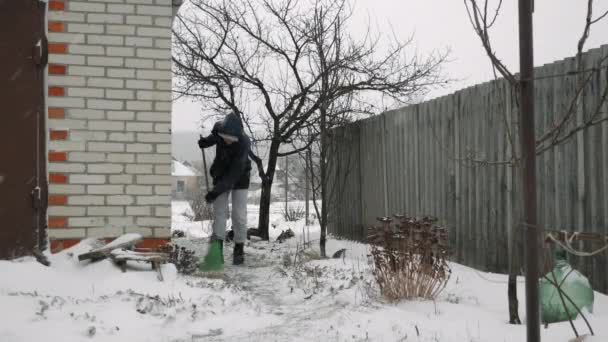 L'uomo spazza la neve dal cortile durante la tempesta di neve. Nevicate. Maschio cancella la neve con scopa — Video Stock
