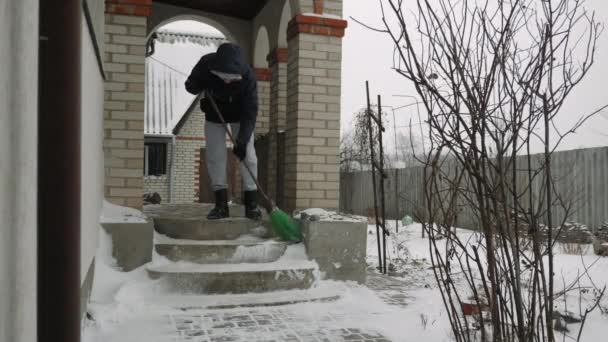 Чоловік піднімає сніг зі сходів біля будинку взимку — стокове відео