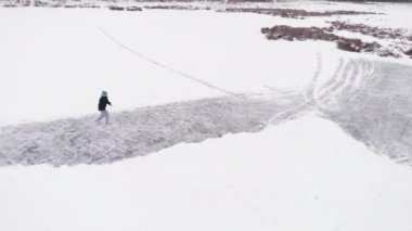 Kışın insan donmuş su deposunda paten kayıyor. Drone donmuş gölün üzerinde uçuyor.