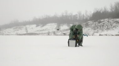 Kışın donmuş buz gölü üzerinde buz matkabı olan adam. Balıkçı gölette buz deliği açıyor.