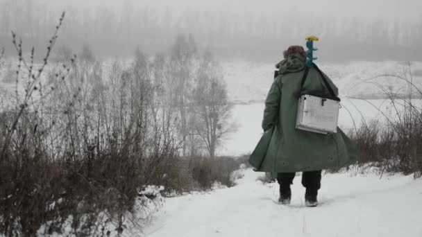 Молодой человек с ледобуром и удочкой находится на замерзшем озере зимой собирается ловить рыбу — стоковое видео