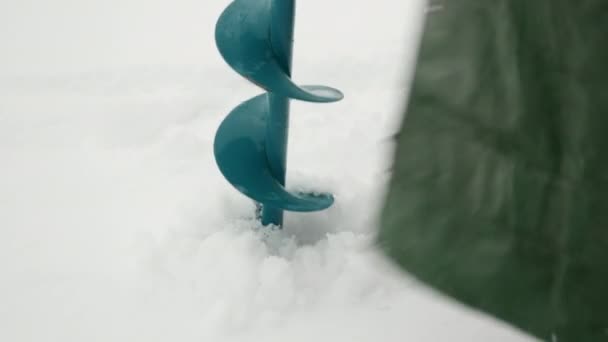 Taladro de hielo en el agujero de hielo. Pescador está perforando agujero en el hielo estanque congelado — Vídeo de stock