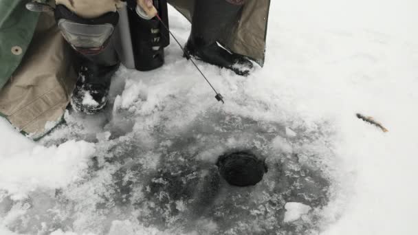 Hombre con caña de pescar es la captura de peces en el agujero de hielo. Pescador está pescando en el lago — Vídeo de stock