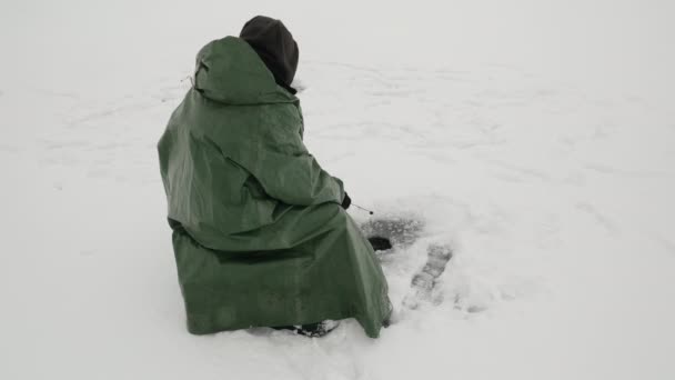 Pesca de Inverno. O homem está a apanhar peixe no buraco de gelo. Pescador com cana de pesca captura peixe — Vídeo de Stock