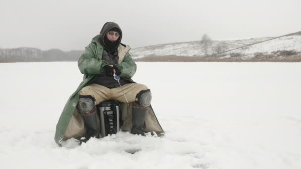 L'homme pêche dans un trou de glace. Pêcheur avec canne à pêche attrape du poisson sur la rivière — Video