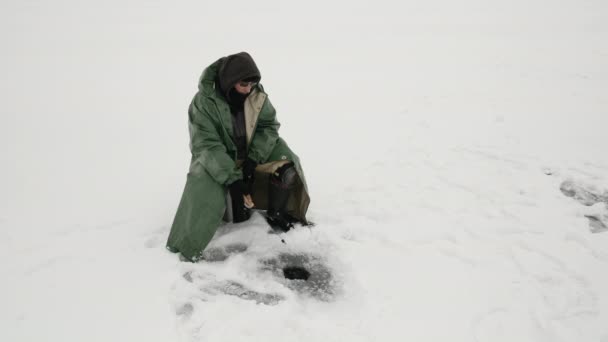 Volwassen man is aan het vissen in een ijsgat. Visser vangt vis op het meer — Stockvideo