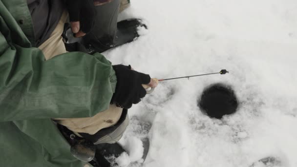 釣竿で凍った湖の氷の穴を閉じます。漁師は池で釣りをしている。 — ストック動画