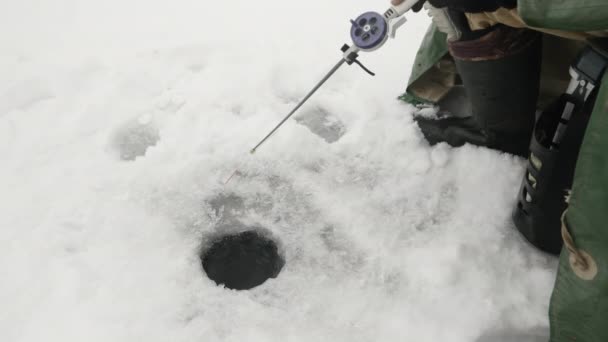 Vara de pesca no buraco de gelo. Homem está pegando peixes em lago congelado no inverno — Vídeo de Stock