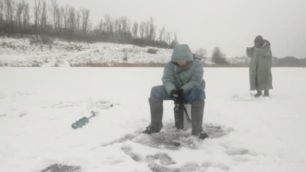 Ψαράς με καλάμι ψαρέματος πιάνει ψάρια στην τρύπα του πάγου. Ο νεαρός ψαρεύει στη λίμνη. — Αρχείο Βίντεο