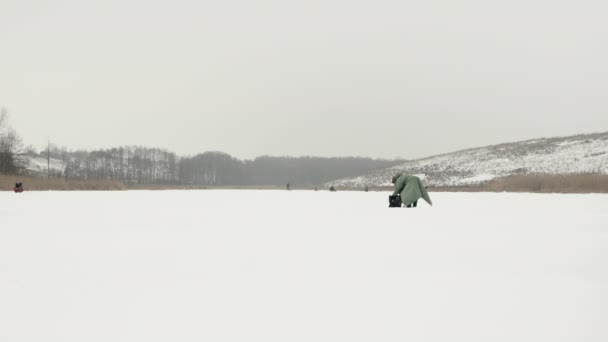冬の釣りの概念。凍った池に氷のドリルを持つ漁師 — ストック動画