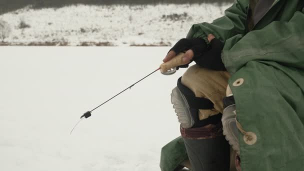 Homme en hiver vêtements extrêmes avec canne à pêche attrape le poisson dans le trou de glace — Video