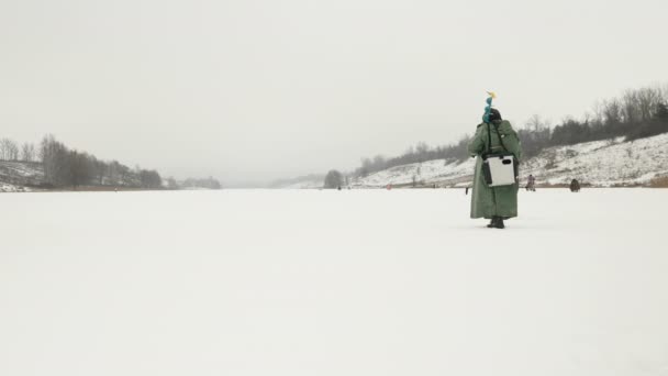 氷のドリルと漁具を持つ漁師は凍った氷の湖に沿って歩いています — ストック動画