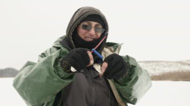 Balıkçı oltadaki balığı çıkarır. İnsan kışın balık tutarken küçük bir balık tutar.