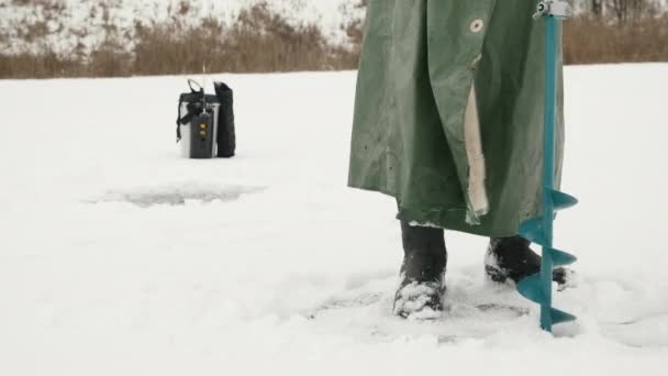 Der Mensch bohrt Eisloch mit Eisbohrer. Fischer macht Eisloch auf See — Stockvideo