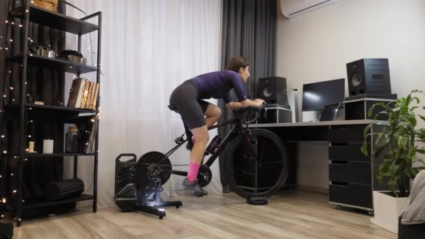साइकिल चालक महिला स्थिर व्यायाम बाइक पर साइकिल चला रही है। घर की गतिविधि। इनडोर साइक्लिंग — स्टॉक वीडियो