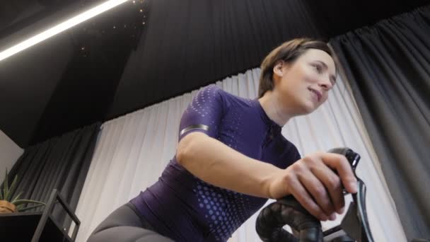 女性は屋内固定自転車でフィットネスカーディオの練習をしています。屋内サイクリング — ストック動画