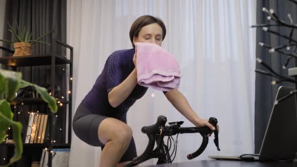 Женщина тренируется на тренере по велоспорту в помещении. Женщина едет на стационарном велосипеде — стоковое видео