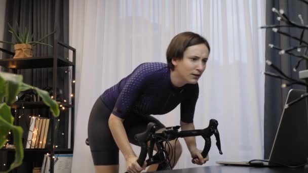 Kvinna avslutar online cykel ras på stationär cykel tränare. Cykling inomhus — Stockvideo