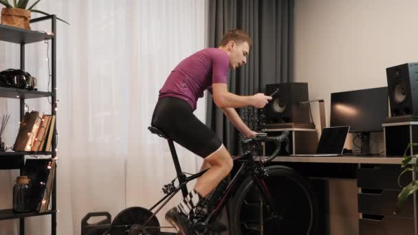 Ο άνθρωπος εκπαιδεύεται σε σταθερό ποδήλατο με smartphone στα χέρια και πληκτρολογώντας μηνύματα — Αρχείο Βίντεο