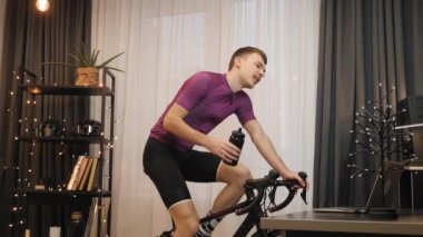 Adam kapalı alanda bisiklet sürerken su içiyor. Akıllı bisiklet eğitmeni. Kapalı alan bisikleti