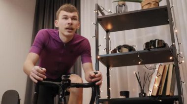 Adam evde bisiklet eğitmeni olarak çok sıkı çalışıyor. Erkek, sıkı kardiyo egzersizleri yapıyor.