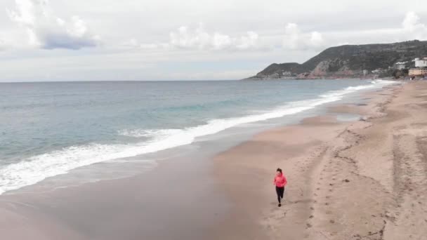 やる気のある女性が海の近くの砂の上を走っている。フィットネス女性は海岸で屋外でジョギングしています — ストック動画