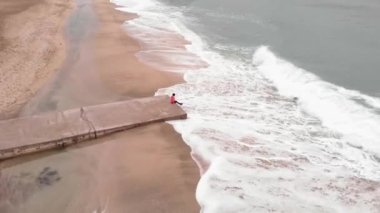 Kadın boş iskelede oturuyor, fırtınada dalgalarla güzel deniz manzarasına hayran.